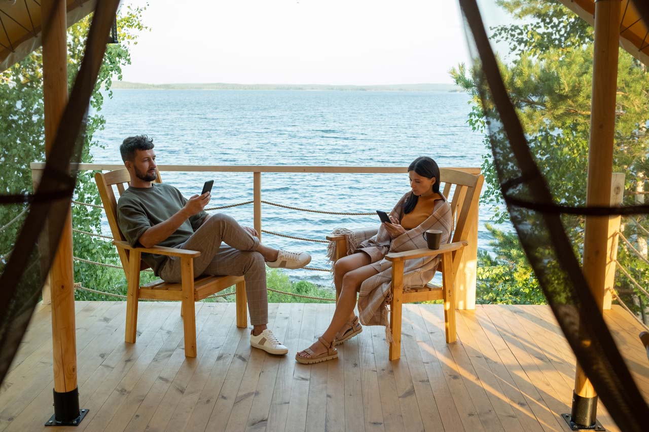 A couple relaxing on a lakeside cabin deck, enjoying a vacation rentals experience.